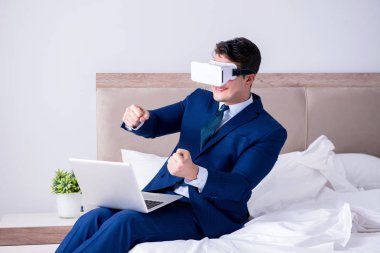 Yatak odasında sanal gerçeklik kulaklığı takan bir iş adamı.