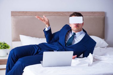 Yatak odasında sanal gerçeklik kulaklığı takan bir iş adamı.