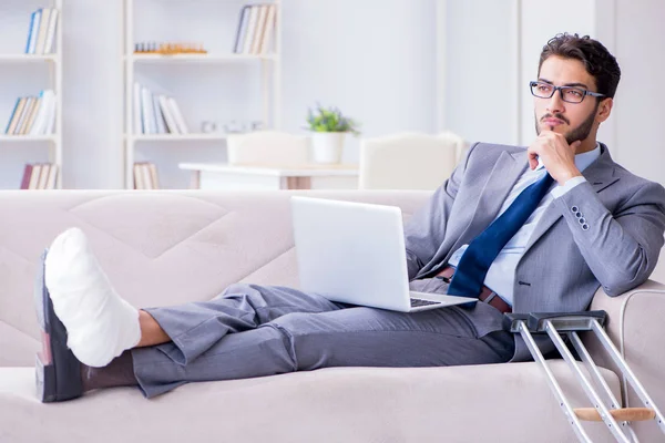 Businessman with crutches and broken leg at home working — Stock Photo, Image