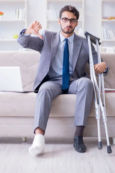 Uomo d'affari con stampelle e gamba rotta a casa che lavora — Foto Stock