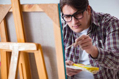 Genç erkek sanatçı parlak stüdyoda resimler çiziyor.