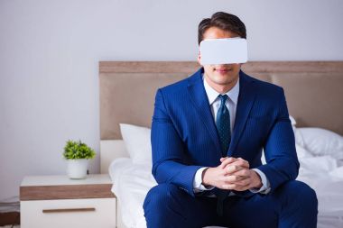 Yatak odasında sanal gerçeklik kulaklığı takan bir iş adamı.