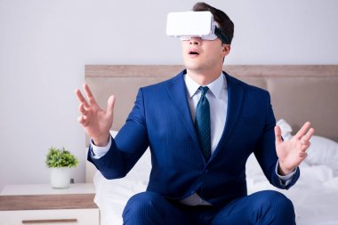Yatak odasında sanal gerçeklik kulaklığı takan bir iş adamı.