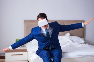Yatak odasında sanal gerçeklik kulaklığı takan bir iş adamı.