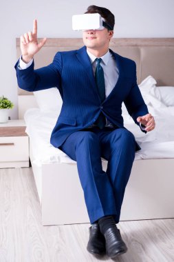 Yatak odasında sanal gerçeklik kulaklığı takan bir iş adamı.