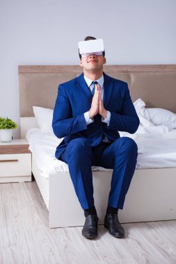 Yatak odasında sanal gerçeklik kulaklığı takan bir iş adamı.