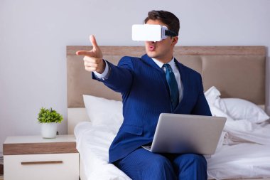 Yatak odasında sanal gerçeklik kulaklığı takan bir iş adamı.