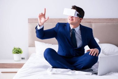 Yatak odasında sanal gerçeklik kulaklığı takan bir iş adamı.