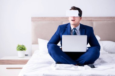 Yatak odasında sanal gerçeklik kulaklığı takan bir iş adamı.