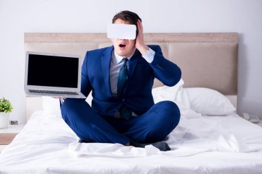 Yatak odasında sanal gerçeklik kulaklığı takan bir iş adamı.
