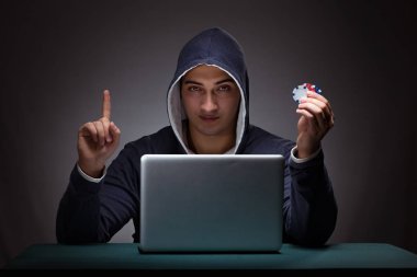 Kapüşonlu genç adam dizüstü bilgisayarın önünde oturuyor.