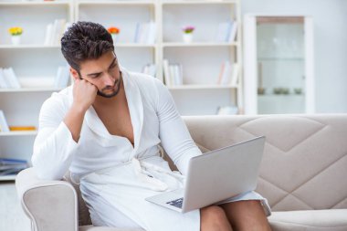 Genç adam evde dizüstü bilgisayarla çalışıyor.