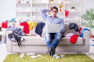 Genç adam dağınık bir odada çalışıyor.