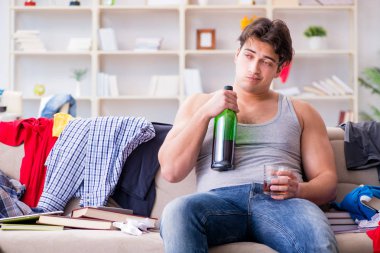 Dağınık bir odada alkol alan genç bir öğrenci.