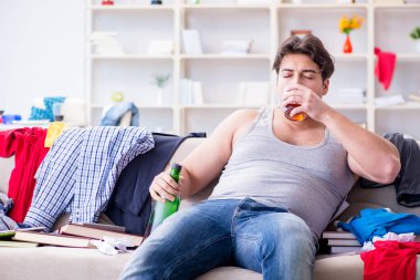 Dağınık bir odada alkol alan genç bir öğrenci.