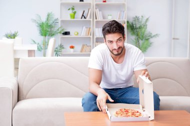 Pizza yiyen adam evde yemek yiyor, dinleniyor.