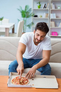 Pizza yiyen adam evde yemek yiyor, dinleniyor.