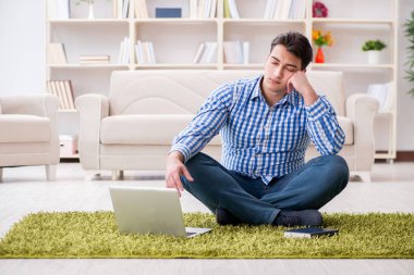 Genç yakışıklı adam evde yerde oturuyor.