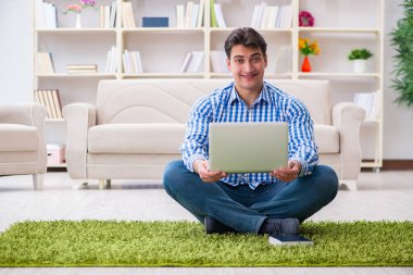 Genç yakışıklı adam evde yerde oturuyor.