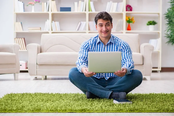 Genç yakışıklı adam evde yerde oturuyor.