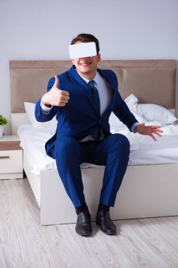 Yatak odasında sanal gerçeklik kulaklığı takan bir iş adamı.