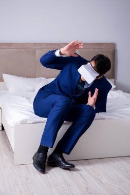 Yatak odasında sanal gerçeklik kulaklığı takan bir iş adamı.