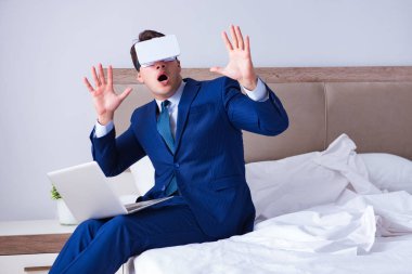 Yatak odasında sanal gerçeklik kulaklığı takan bir iş adamı.