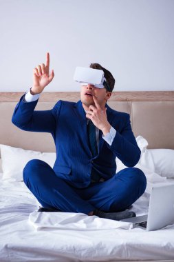 Yatak odasında sanal gerçeklik kulaklığı takan bir iş adamı.