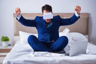 Yatak odasında sanal gerçeklik kulaklığı takan bir iş adamı.