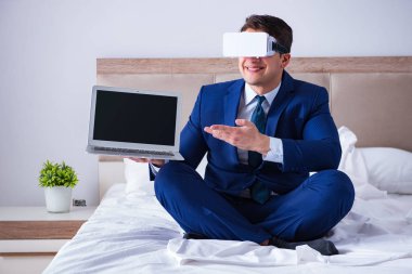 Yatak odasında sanal gerçeklik kulaklığı takan bir iş adamı.