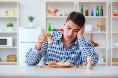 Genç koca öğle yemeğinde tatsız yemekler yiyor.