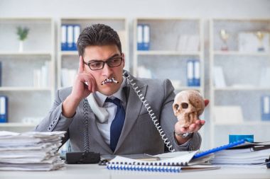 Ofisteki işadamı elinde insan kafatasıyla sigara içiyor.