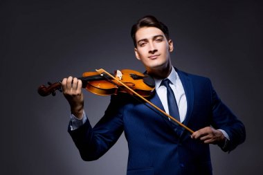 Genç adam karanlık odada keman çalıyor.