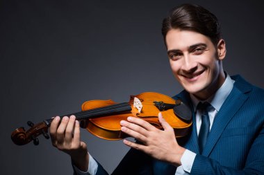 Genç adam karanlık odada keman çalıyor.