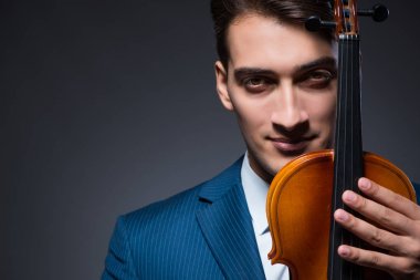 Genç adam karanlık odada keman çalıyor.