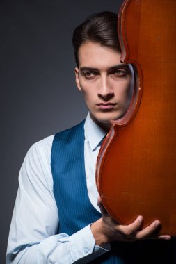 Genç adam karanlık odada çello çalıyor.