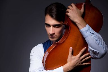 Genç adam karanlık odada çello çalıyor.