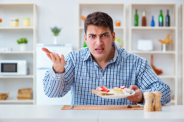 Молодой муж ест безвкусную еду дома на обед — стоковое фото