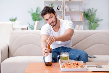 Pizza yiyen adam evde yemek yiyor, dinleniyor.