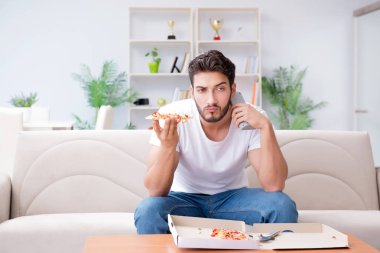 Pizza yiyen adam evde yemek yiyor, dinleniyor.