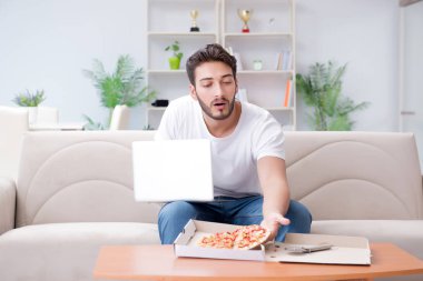 Pizza yiyen adam evde yemek yiyor, dinleniyor.