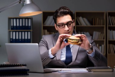Gece geç saatte iş adamı hamburger yiyor.