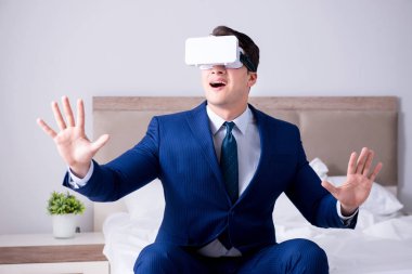 Yatak odasında sanal gerçeklik kulaklığı takan bir iş adamı.