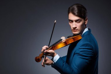 Genç adam karanlık odada keman çalıyor.