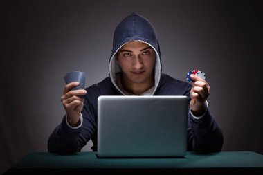 Kapüşonlu genç adam dizüstü bilgisayarın önünde oturuyor.