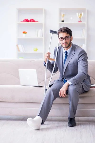 Uomo d'affari con stampelle e gamba rotta a casa che lavora — Foto Stock