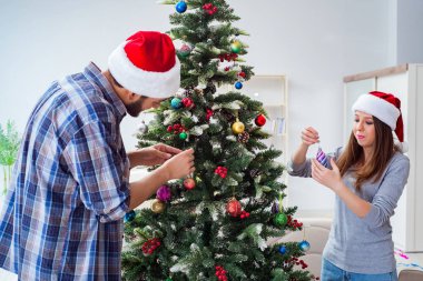 Genç aile Noel ağacını mutlu bir vesileyle süslüyor.