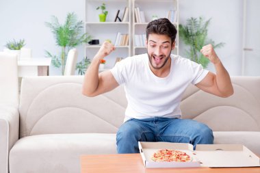 Pizza yiyen adam evde yemek yiyor, dinleniyor.