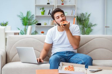 Pizza yiyen adam evde yemek yiyor, dinleniyor.