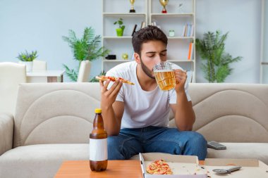 Pizza yiyen adam evde yemek yiyor, dinleniyor.